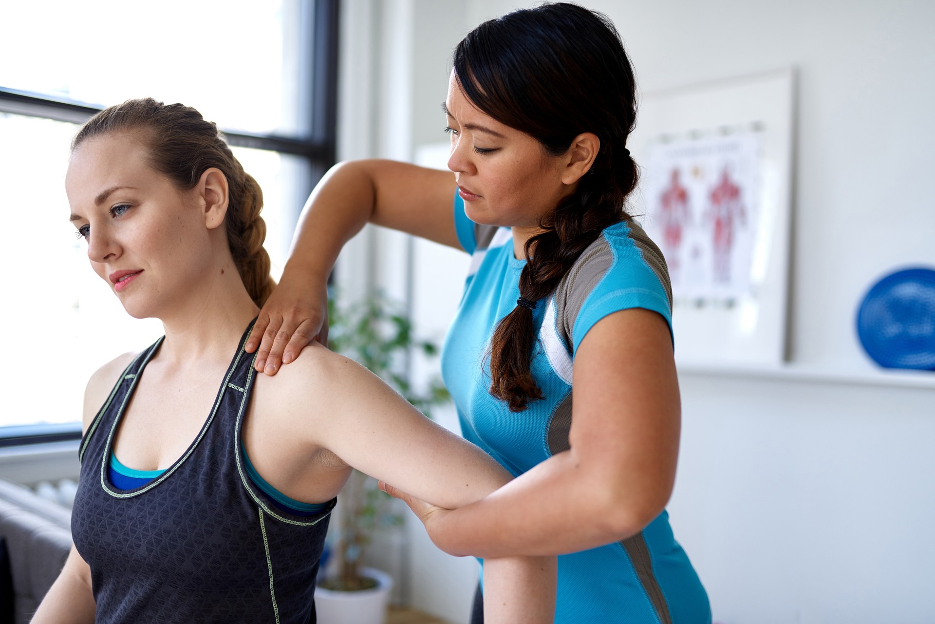 Chinese woman physiotherapy professional giving a treatment to an attractive blond client in a bright medical office