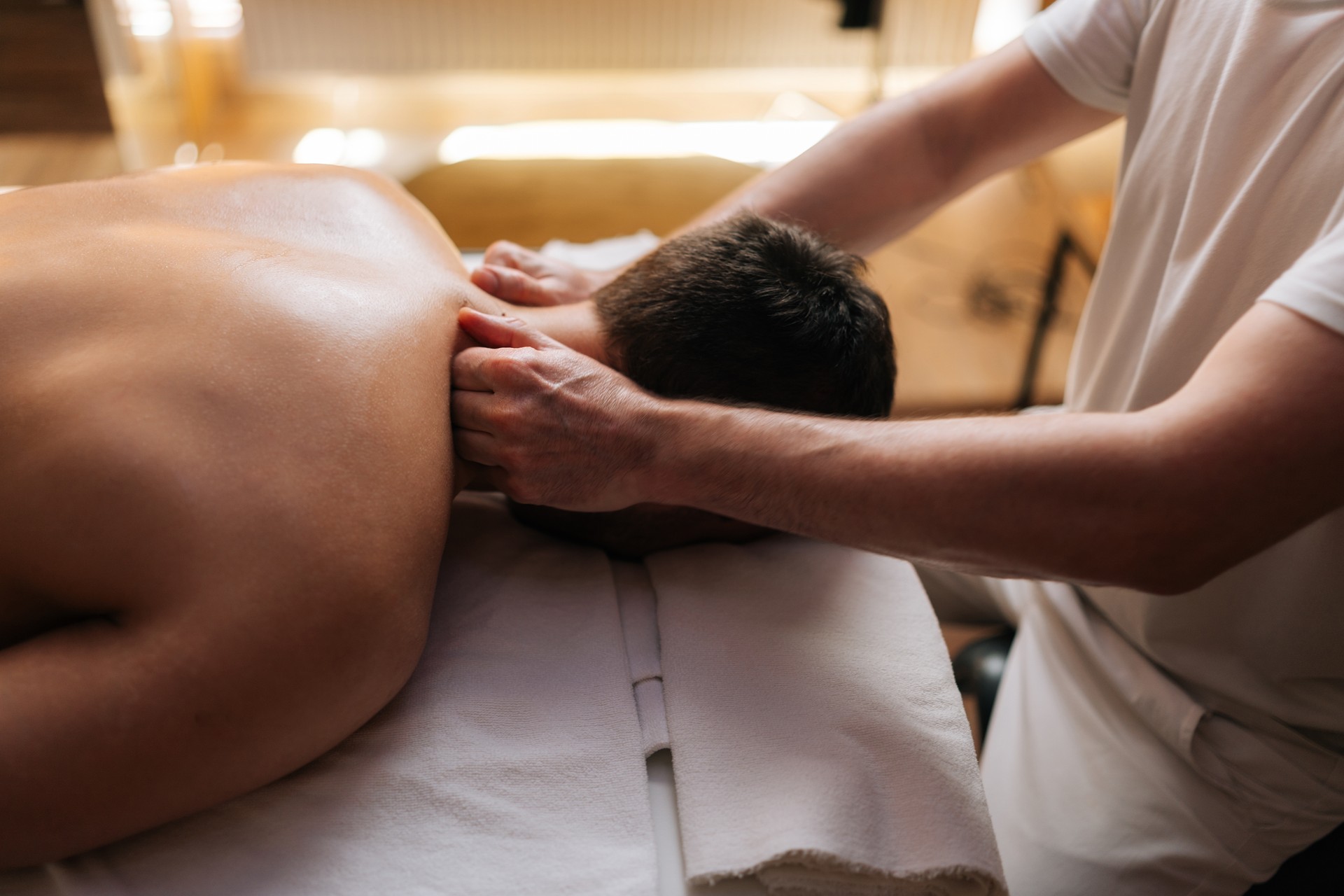 Closeup side view head of unrecognizable young relaxed man lying down on massage table during shoulder and neck massage at spa salon.